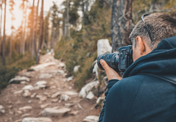 Fotograaf man houdt een camera in een bos. - Foto, afbeelding
