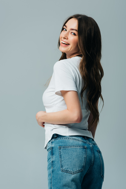 happy beautiful girl in white t-shirt and jeans looking at camera isolated on grey - Photo, Image