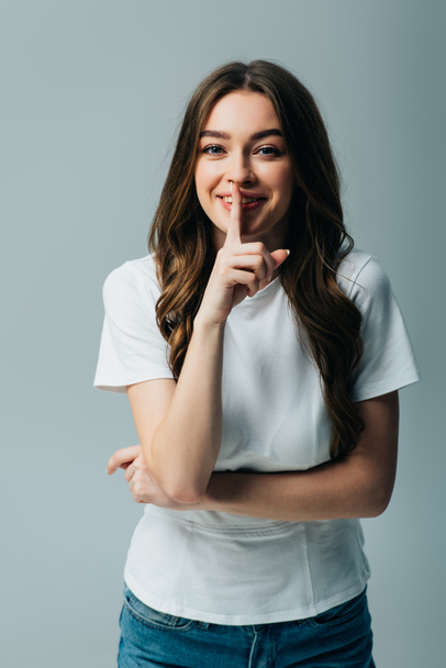 happy beautiful girl in white t-shirt showing shh sign isolated on grey - Foto, immagini