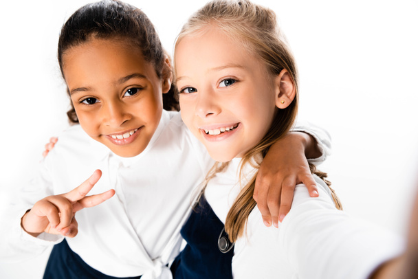 selective focus of cheerful african american schoolgirl showing victory sign while hugging friend isolated on white - Fotografie, Obrázek