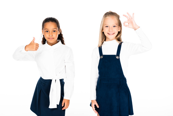 cute african american schoolgirl showing thumb up near multicultural friend showing ok gesture isolated on white - Photo, Image