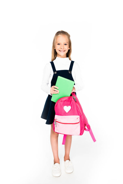 full length view of cute schoolgirl holding backpack and book on white background - Foto, Imagen