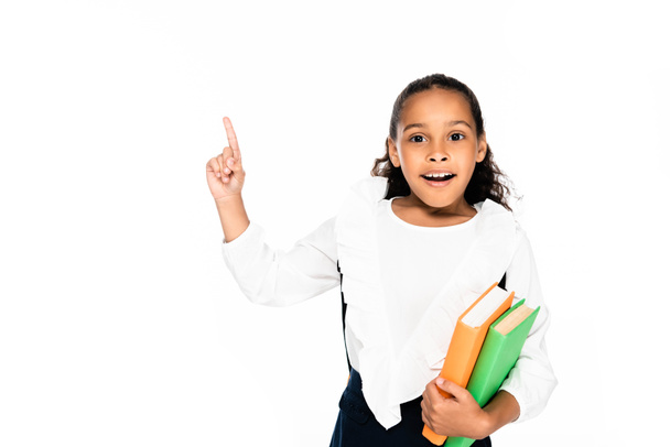 cheerful african american schoolgirl pointing with finger while holding books isolated on white - Foto, Imagen