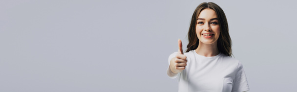 panoramic shot of happy beautiful girl in white t-shirt showing thumb up isolated on grey - Fotoğraf, Görsel