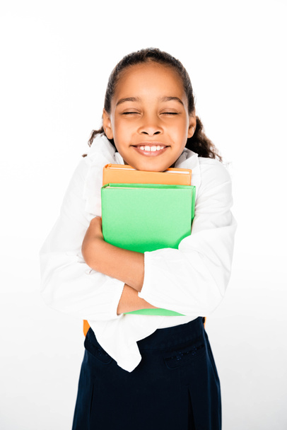 heureuse écolière afro-américaine tenant des livres et souriant avec les yeux fermés sur fond blanc
 - Photo, image