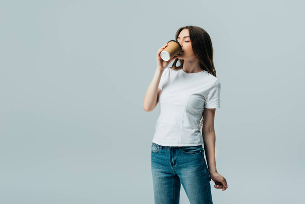schönes Mädchen im weißen T-Shirt mit geschlossenen Augen trinkt aus Pappbecher isoliert auf grau - Foto, Bild