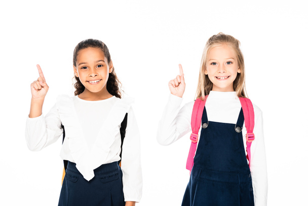 two cheerful multicultural schoolgirls showing idea gestures while smiling at camera isolated on white - Fotoğraf, Görsel