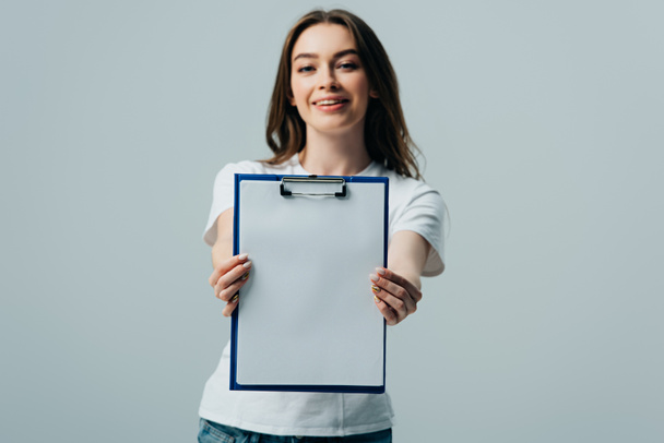 happy beautiful girl in white t-shirt presenting blank clipboard isolated on grey - Fotografie, Obrázek