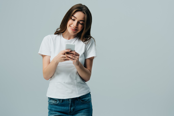 happy beautiful girl in white t-shirt using smartphone isolated on grey - Photo, Image