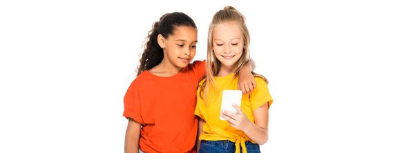 panoramic shot of cute african american kid hugging friend using smartphone isolated on white - Zdjęcie, obraz