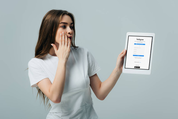KYIV, UKRAINE - JUNE 6, 2019: shocked beautiful girl in white t-shirt showing digital tablet with Instagram app isolated on grey - Φωτογραφία, εικόνα