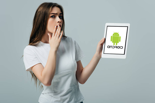 KYIV, UKRAINE - JUNE 6, 2019: shocked beautiful girl in white t-shirt showing digital tablet with android logo isolated on grey - Foto, imagen