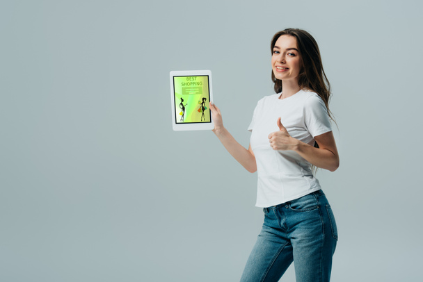 sorrindo menina bonita em t-shirt branca mostrando tablet digital com aplicativo de compras on-line e mostrando polegar para cima isolado em cinza
 - Foto, Imagem