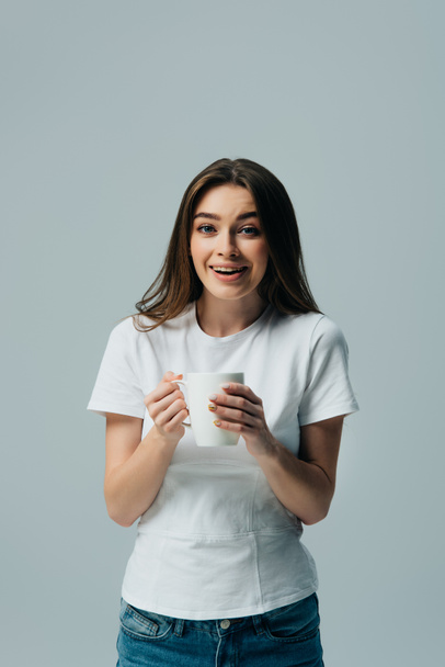 excited smiling girl in white t-shirt holding white mug isolated on grey - Photo, Image