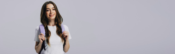 Panoramaaufnahme einer lächelnden hübschen Studentin mit Rucksack isoliert auf grau - Foto, Bild