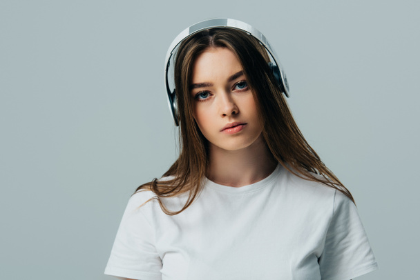 serious pretty girl listening music in wireless headphones isolated on grey - Foto, afbeelding