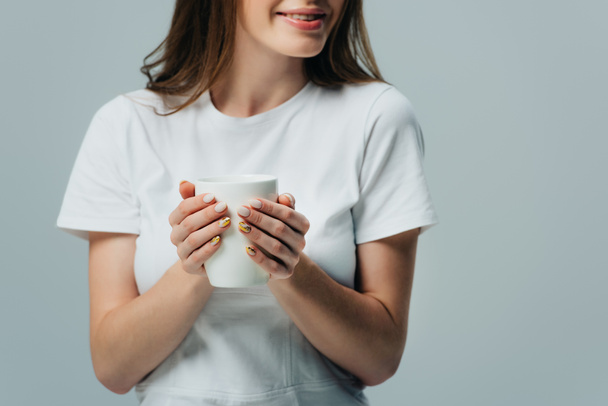 cropped view of smiling girl in white t-shirt holding white mug isolated on grey - Фото, изображение