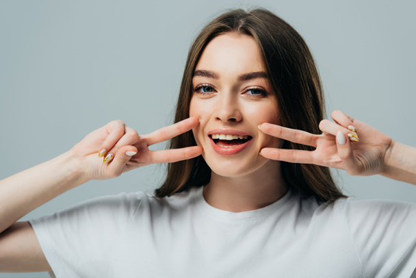 beautiful happy girl showing peace signs near face isolated on grey - Foto, Imagen