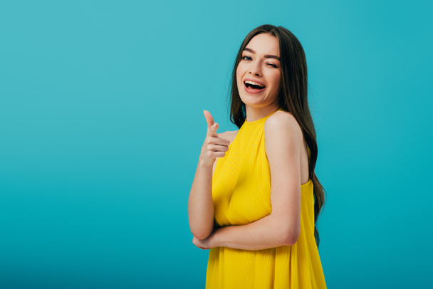 happy beautiful girl in yellow dress pointing with finger at camera and winking isolated on turquoise - Φωτογραφία, εικόνα