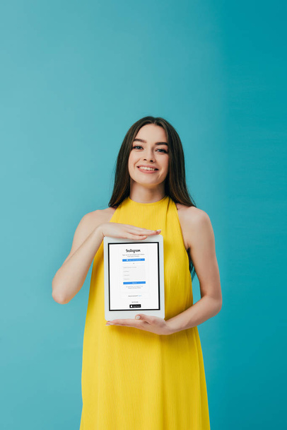 KYIV, UKRAINE - JUNE 6, 2019: happy beautiful girl in yellow dress showing digital tablet with instagram app isolated on turquoise - Zdjęcie, obraz