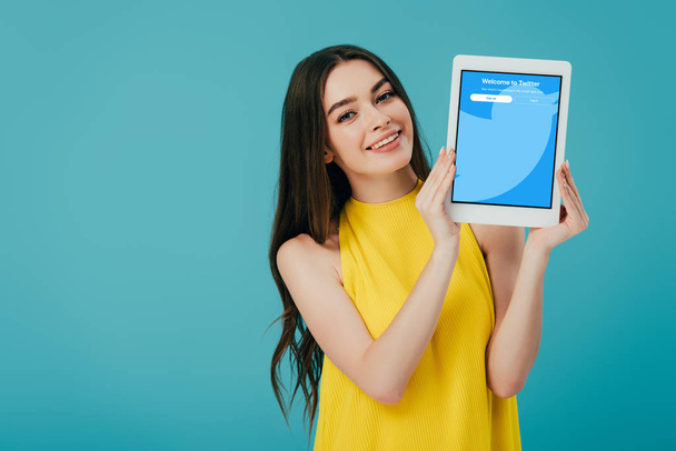 KYIV, UKRAINE - JUNE 6, 2019: happy beautiful girl in yellow dress showing digital tablet with twitter app isolated on turquoise - Foto, Imagen