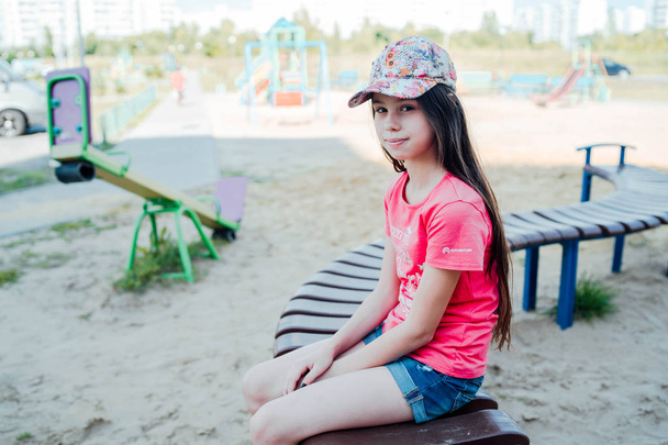 Egy lány, hosszú, Sötét haja alkalmi ruhák ül egy padon a játszótéren. - Fotó, kép