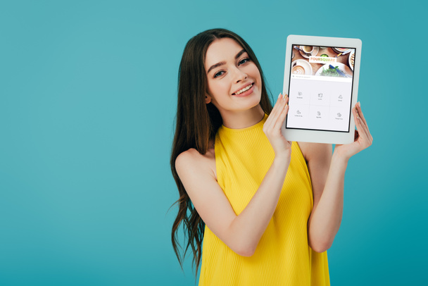 KYIV, UKRAINE - JUNE 6, 2019: happy beautiful girl in yellow dress showing digital tablet with forsquare app isolated on turquoise - Fotoğraf, Görsel