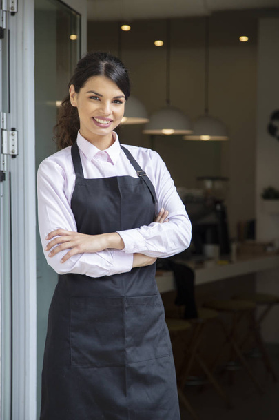 Beautiful waitress in apron smiling, showing welcome to coffee shop - Фото, изображение