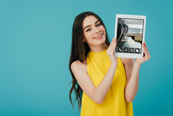 beautiful girl in yellow dress showing digital tablet with tickets app isolated on turquoise - Foto, Imagen