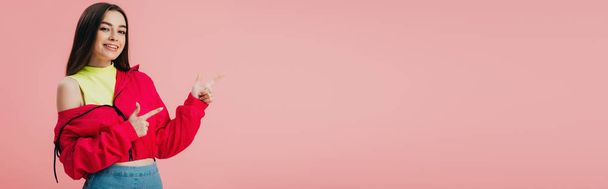hermosa chica sonriente en ropa brillante señalando con los dedos en el espacio de copia aislado en rosa, plano panorámico
 - Foto, imagen