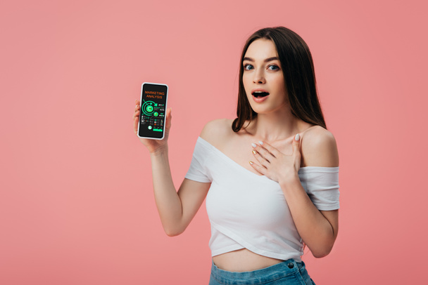 beautiful shocked girl holding smartphone with marketing analysis app isolated on pink - Photo, Image