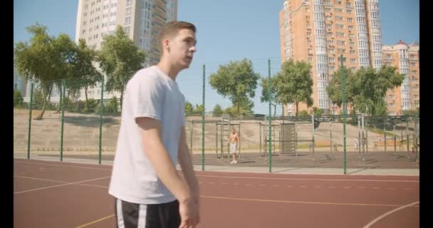 Closeup portré fiatal kaukázusi férfi kosárlabda játékos dobott egy labdát a karika a bíróság cityscrapes a háttérben - Felvétel, videó