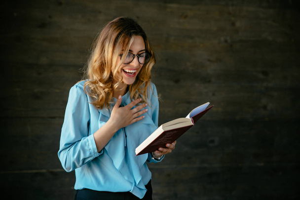 Attractive woman laughing after reading a funny joke in book. - Φωτογραφία, εικόνα