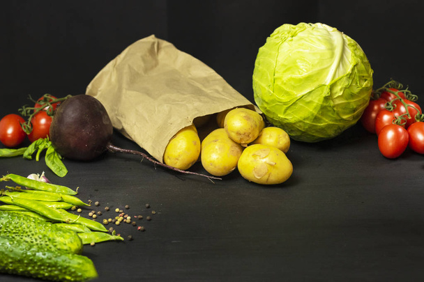 Fresh, organic vegetables: potatoes, tomatoes, garlic, cabbage, beets, cucumbers, peas, pepper on a black background. Healthy food concept, plant background, natural eco-products, organic food - Photo, Image