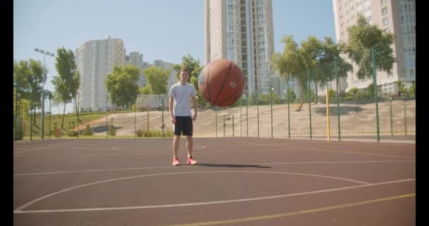 Closeup portrait of caucasian male basketball player throwing ball in hoop on court with buildings on the background - Кадри, відео