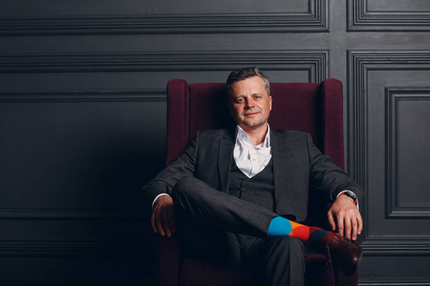 Portrait of sitting chair businessman in strict gray suit and colorful multi colored socks. Business and success concept. - Photo, Image