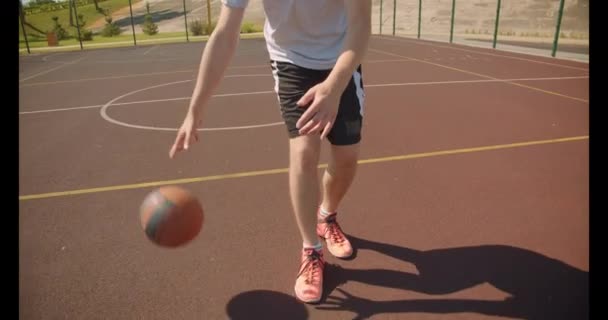 Closeup portrait of young attractive caucasian male basketball player throwing a ball in the hoop on the court in the park - Imágenes, Vídeo