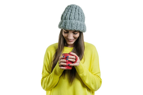 Winter portrait of young smiling positive woman in sweater, knitted hat with mug of hot drink, white background isolated - Photo, image