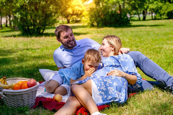 ευτυχισμένη οικογένεια στην κουβέρτα αναπαύεται στο πάρκο, έγκυος μητέρα. - Φωτογραφία, εικόνα