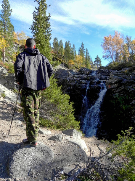 A man in a black jacket from the back against the backdrop of a waterfall in the fall - Foto, Imagen