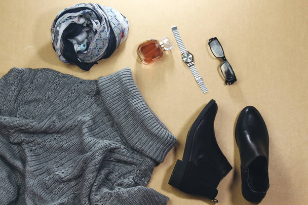 Damenherbstgarnitur, Winterbekleidung: grauer Pullover in Übergröße, schwarze Stiefel und Hijab-Schal, Glasparfümflasche, silberne Handuhr, Brille. modische Kleidung für Spaziergänge, flache Lage - Foto, Bild