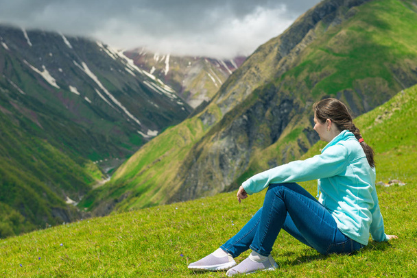 Uma mulher senta-se na grama e admira a bela montanha lan
 - Foto, Imagem