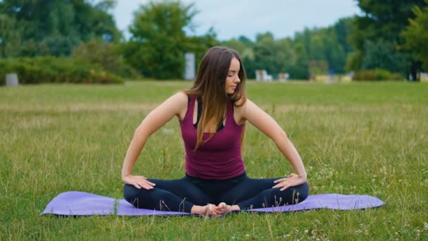 夏の公園で野外トレーニング中に瞑想する若い美しい女性は、彼女は平和を感じています。朝にヨガを屋外でやるスポーティな女の子. - 映像、動画