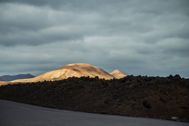incredibly beautiful volcanoc landscape with black sand and red mountains and a beautiful sky during the day on the spanish island of Canary Lanzarote - Photo, Image