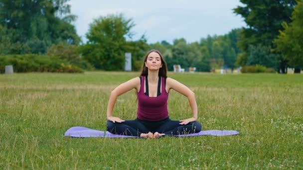Jonge blanke vrouw ontspannen door het beoefenen van yoga op de buitenplaats in de ochtend. Mooie vrouw doet yoga in het Park op groen gras - Video