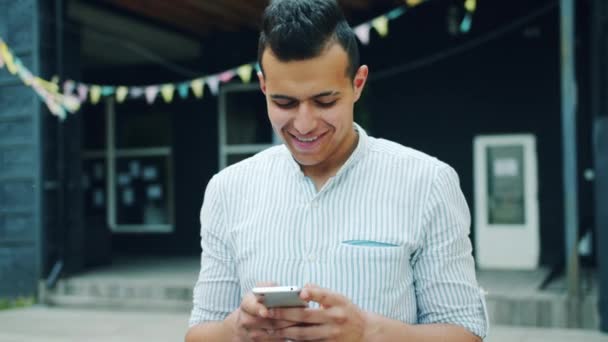 Portré vonzó Arab férfi segítségével okostelefon megható képernyő szabadban - Felvétel, videó