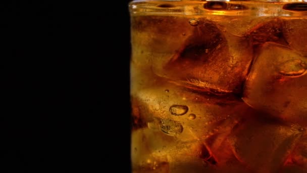 ガラスの氷と泡を持つコーラは黒で回転します - 映像、動画
