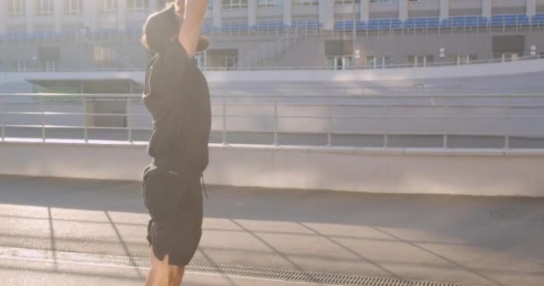 Closeup portrait of adult caucasian sporty male jogger stretching arms on the stadium in the urban city outdoors - Filmati, video