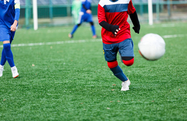 Garçons en vêtements de sport rouges et bleus joue au football sur le terrain, dribble ball. Jeunes joueurs de football avec ballon sur herbe verte. Entraînement, football, mode de vie actif pour les enfants
  - Photo, image
