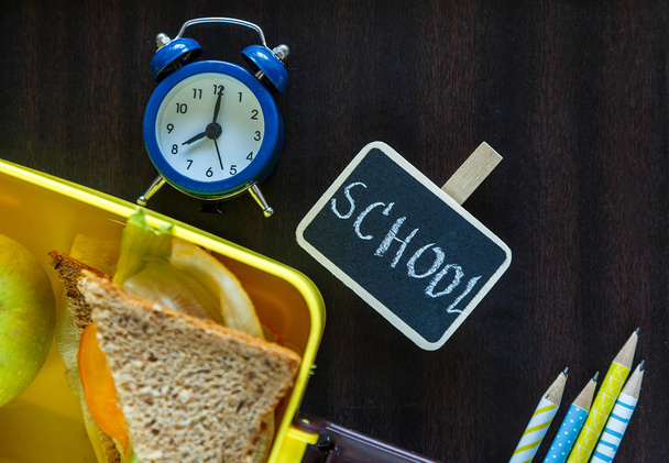 Σχολείο μπλε κουτί μεσημεριανό με σπιτικά σάντουιτς, πράσινο μήλο, μπισκότα, μολύβια, ρολόι, σημειωματάρια στο τραπέζι. Υγιεινό φαγητό στο σχολείο. Πίσω στο σχολικό υπόβαθρο. Επίπεδη όψη, κορυφή θέα. - Φωτογραφία, εικόνα